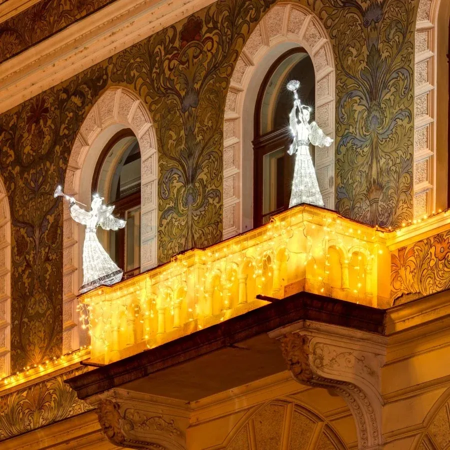 Jégfehér trombitás LED angyalok egy történelmi homlokzat erkélyén meleg fehér fényjégcsapokkal